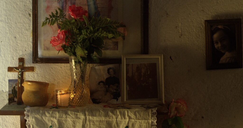 Une table avec des cadres photos, un vase de fleurs et une croix de Jesus